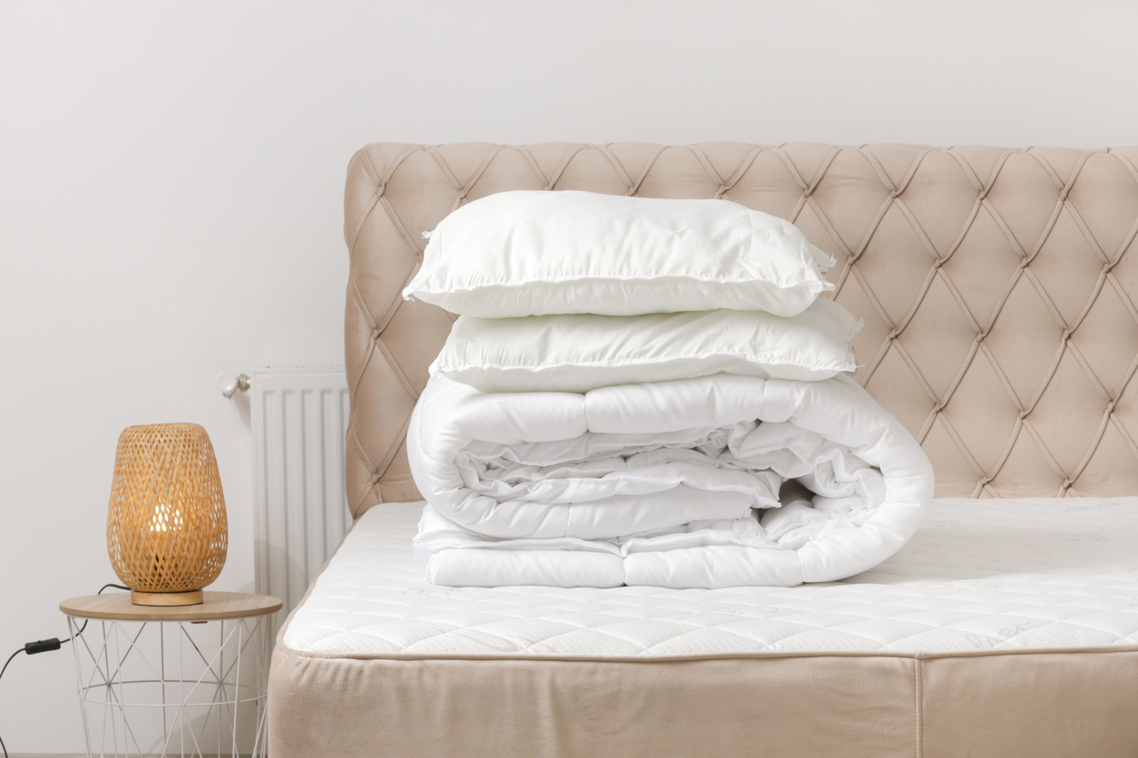 Freshly washed white comforter and pillows stacked on a bed, illustrating clean results after using a laundromat to wash comforters.