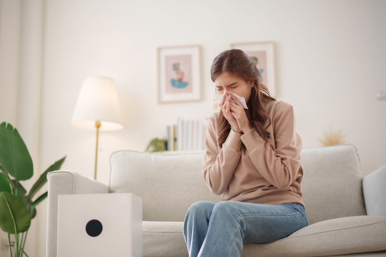 Young woman sneezing at home from allergies, reminder of why it’s important to wash clothes for allergies in Nashville.
